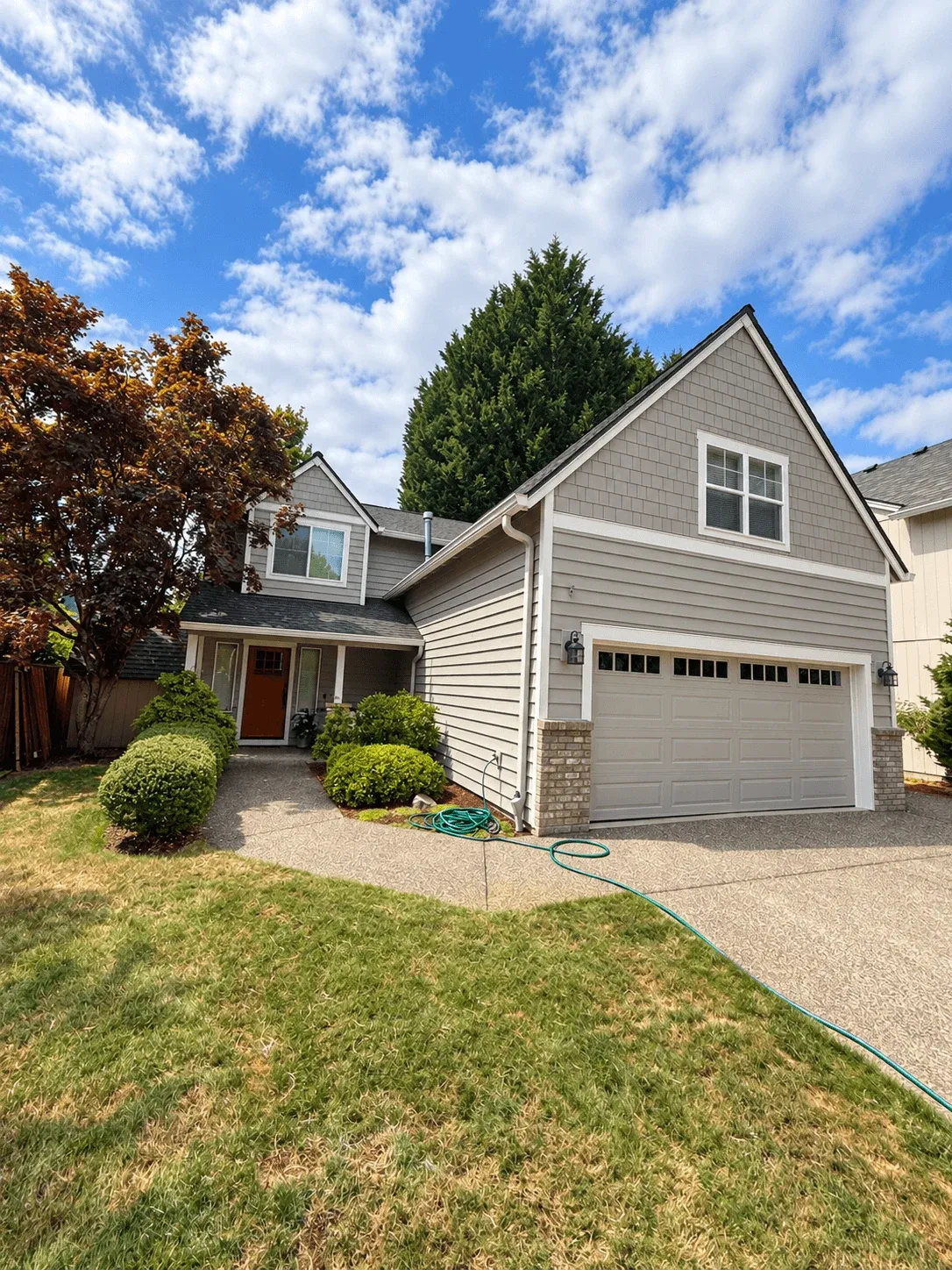 Gray lap siding and shake gable over a garage with a brick base